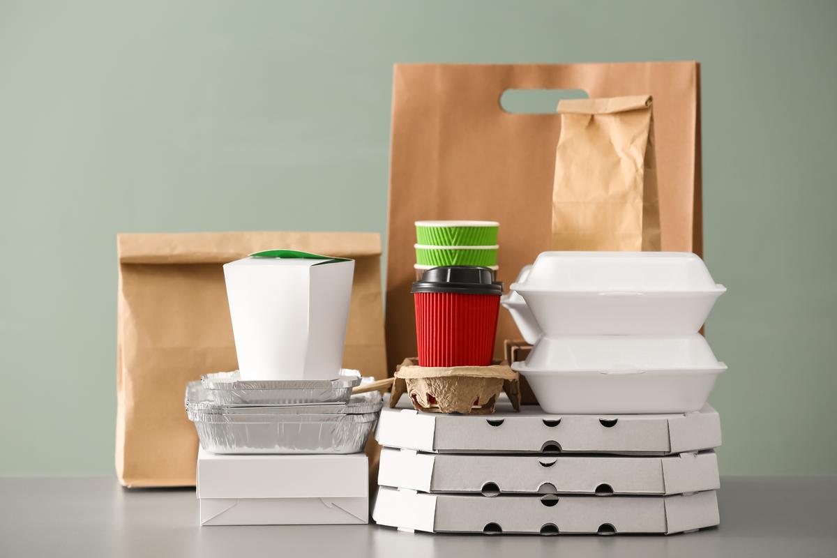 A display of different types of food packaging including pizza boxes, take away containers, aluminum trays, paper cups and paper bags on a counter table.
